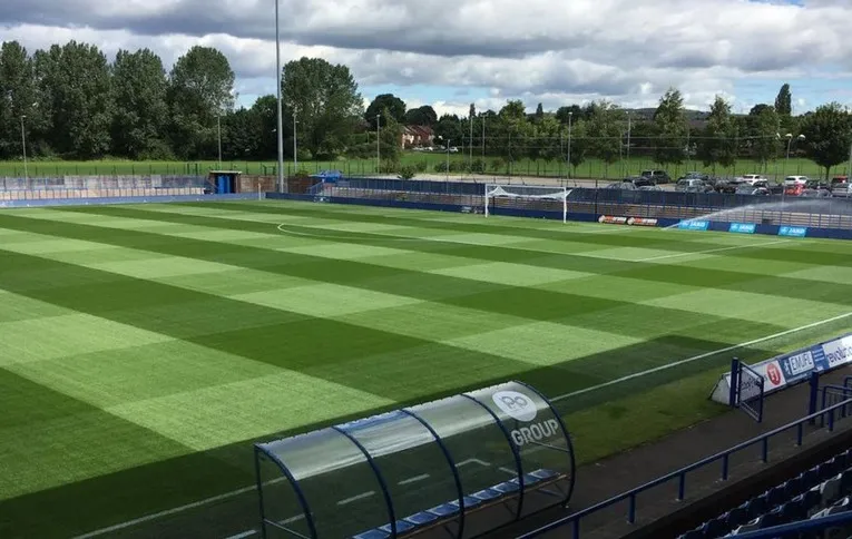 Góc nhìn từ khán đài chính tại sân Tameside, bao quát toàn bộ mặt cỏ và các khu vực thi đấu.