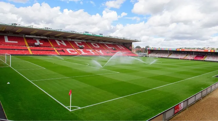 Khung cảnh sân Sincil Bank nhìn từ khán đài, mặt sân cỏ xanh mướt và khán đài trống.