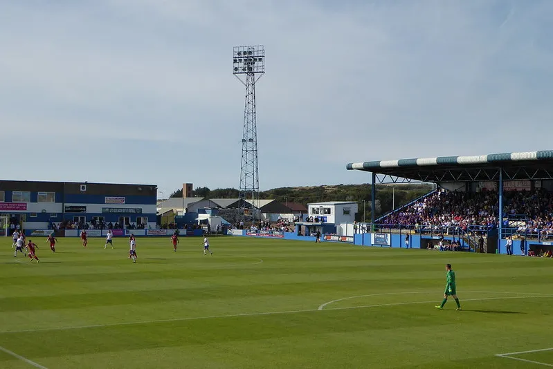 Một trận đấu sôi động đang diễn ra tại sân Holker Street, sân nhà của Barrow AFC