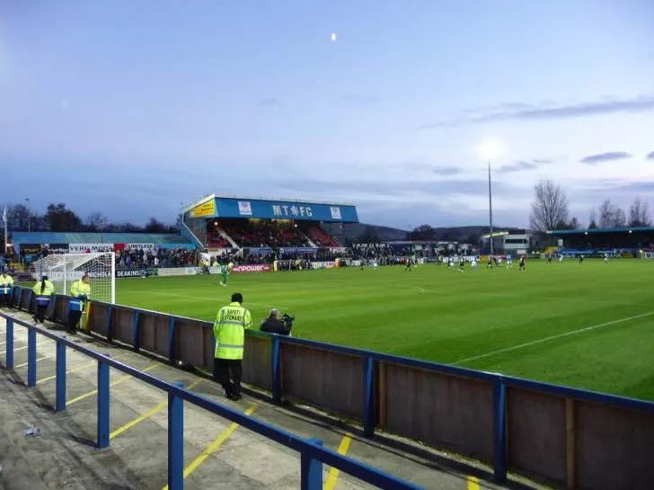 Trận đấu tại sân Moss Rose vào ban đêm, tập trung vào khán đài Silk FM của Macclesfield Town